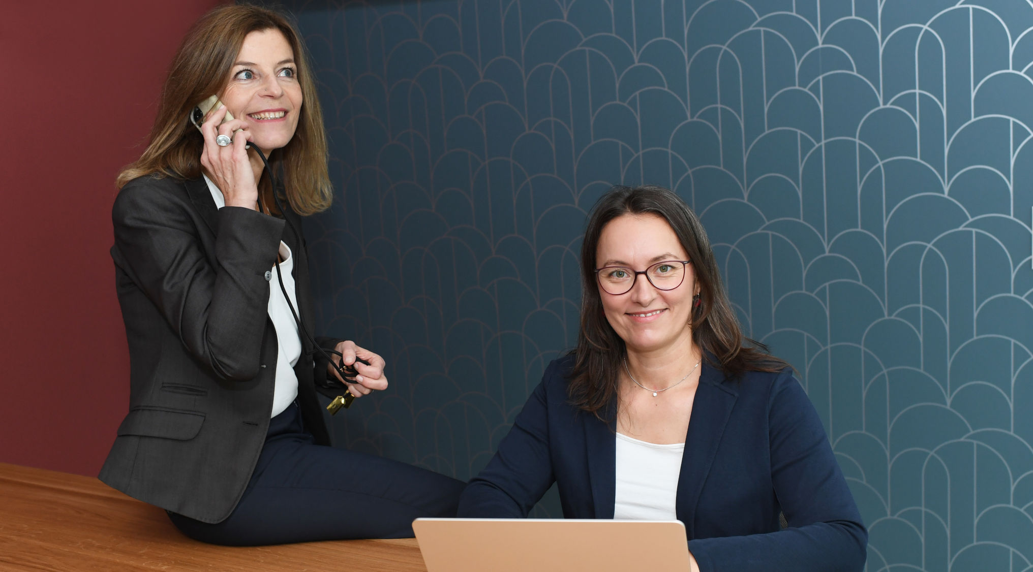 Manuela Langos sitzt am Computer und Sabine Zeilinger telfoniert