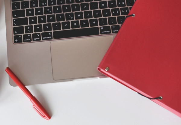 Auf einer Laptoptastatur liegt ein roter Ordner und ein roter Stift