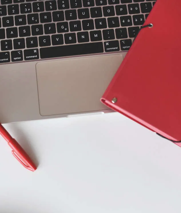 Auf einer Laptoptastatur liegt ein roter Ordner und ein roter Stift